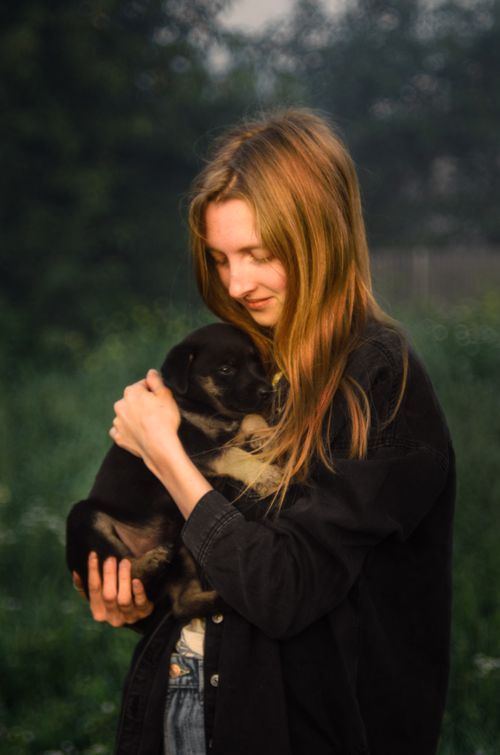 Free A young woman lovingly cradles a cute puppy in an outdoor setting, surrounded by greenery. Stock Photo