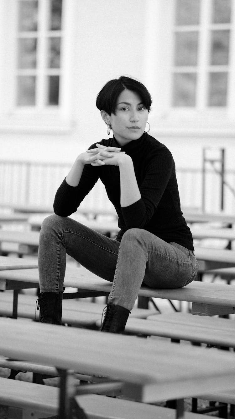 Brunette Woman In Black Sweater And Jeans Sitting On A Street Cafe Table