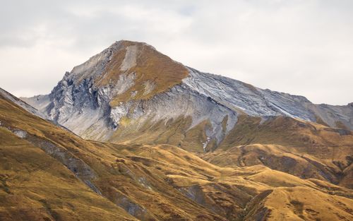 Free Scenic view of a rugged mountain peak surrounded by rolling hills under a cloudy sky. Stock Photo
