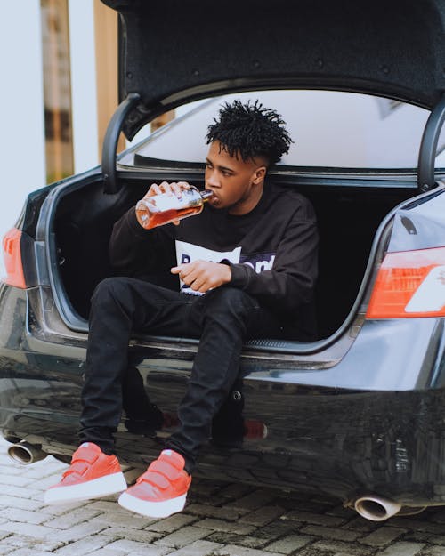 Man Drinking Alcohol and Sitting in Car Trunk