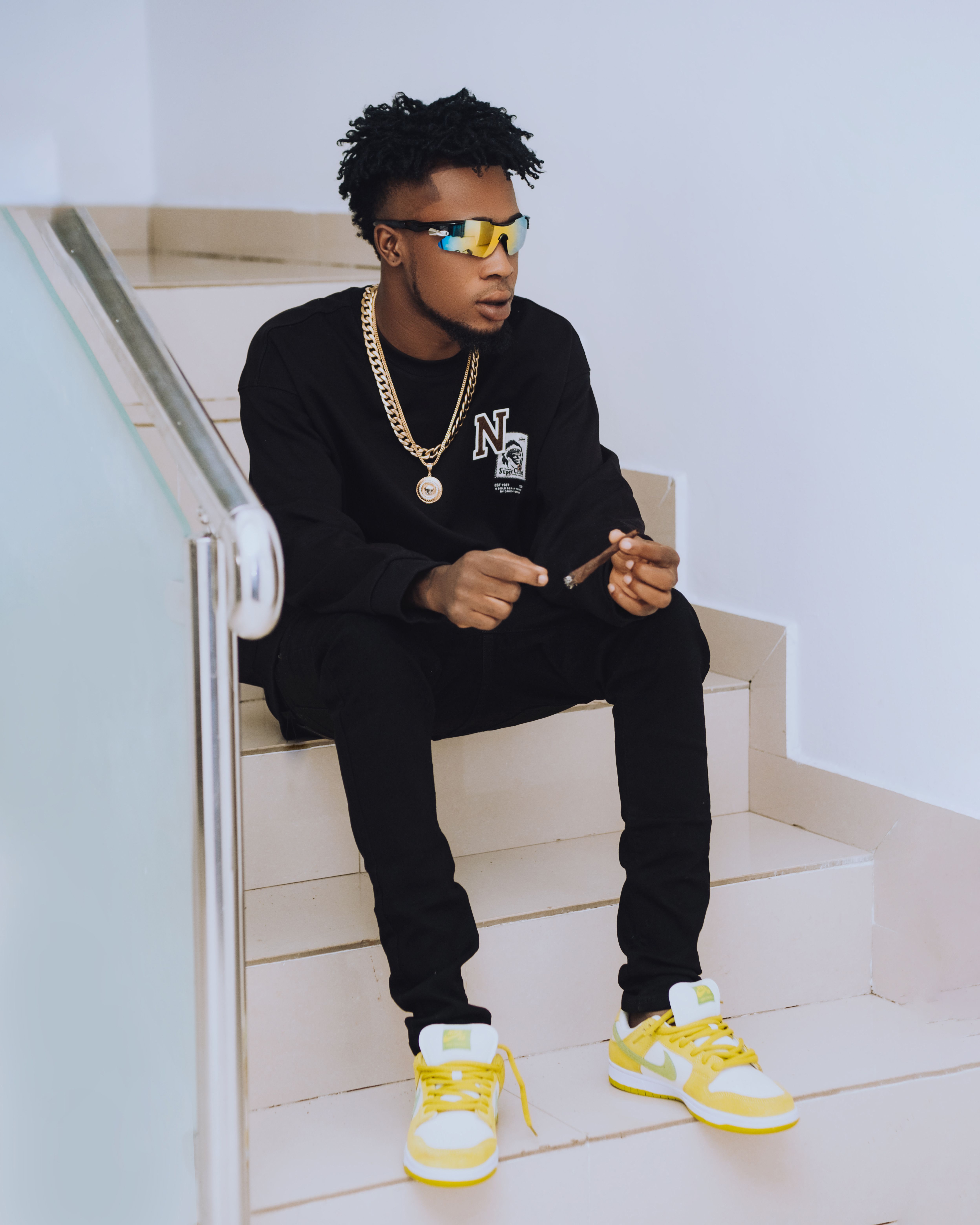 Fashionable young man in sunglasses and casual wear sitting on indoor stairs, exuding confidence.