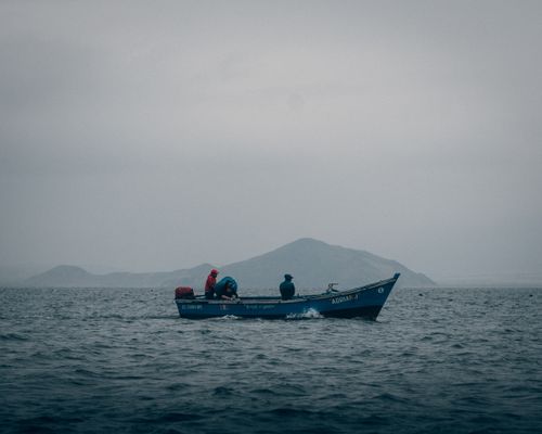 Free Fishermen on a motorboat amidst misty waters and distant mountains, creating a tranquil scene. Stock Photo