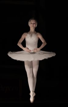 Elegant ballet dancer in white tutu performing in a studio with a dark background.