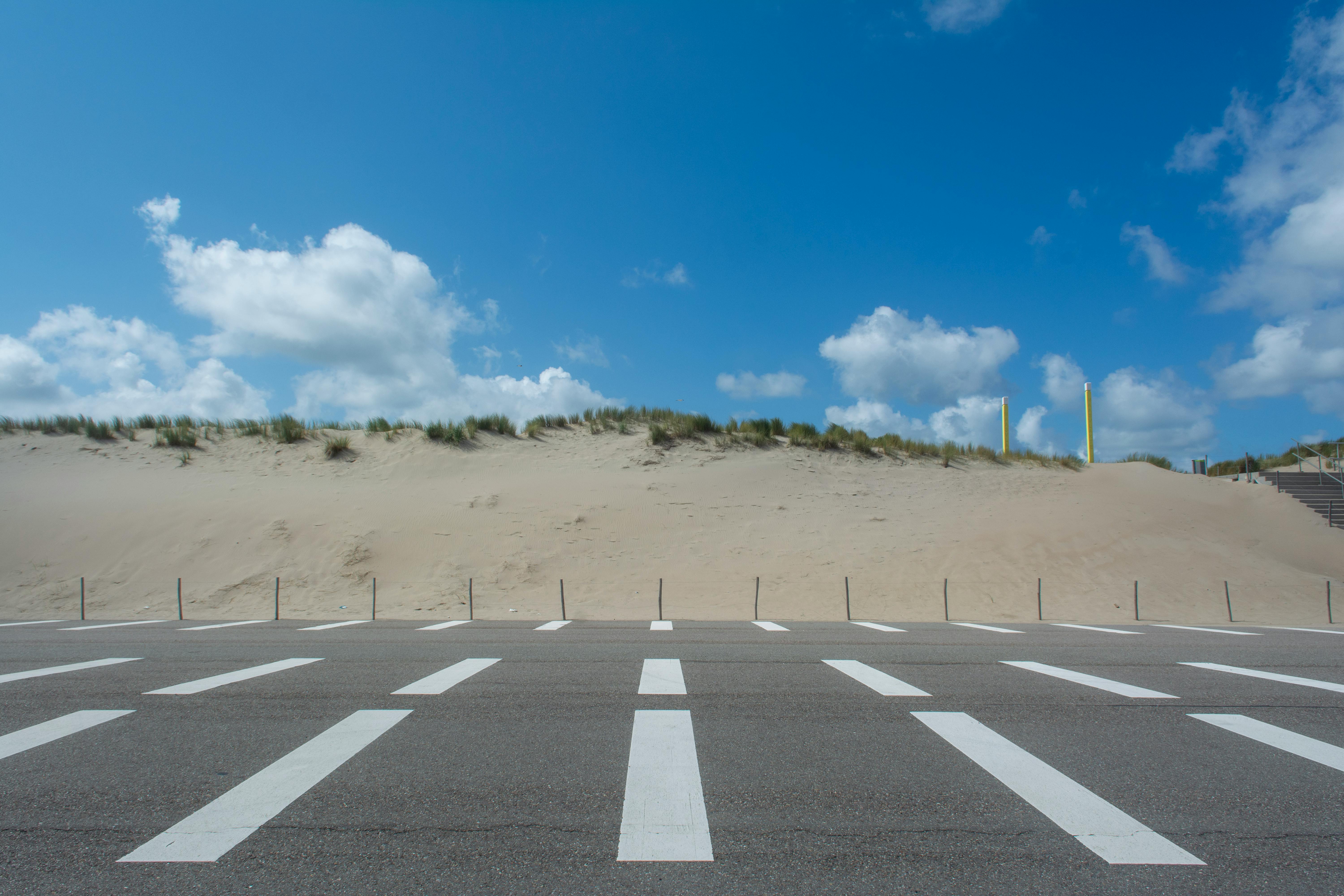 Empty road with sand dunes under a bright blue sky at Maasvlakte Rotterdam.