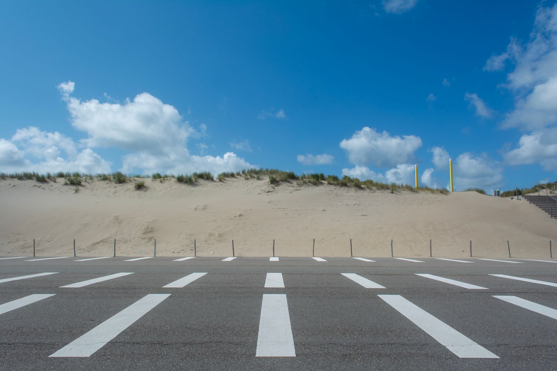 Empty road with sand dunes under a bright blue sky at Maasvlakte Rotterdam.