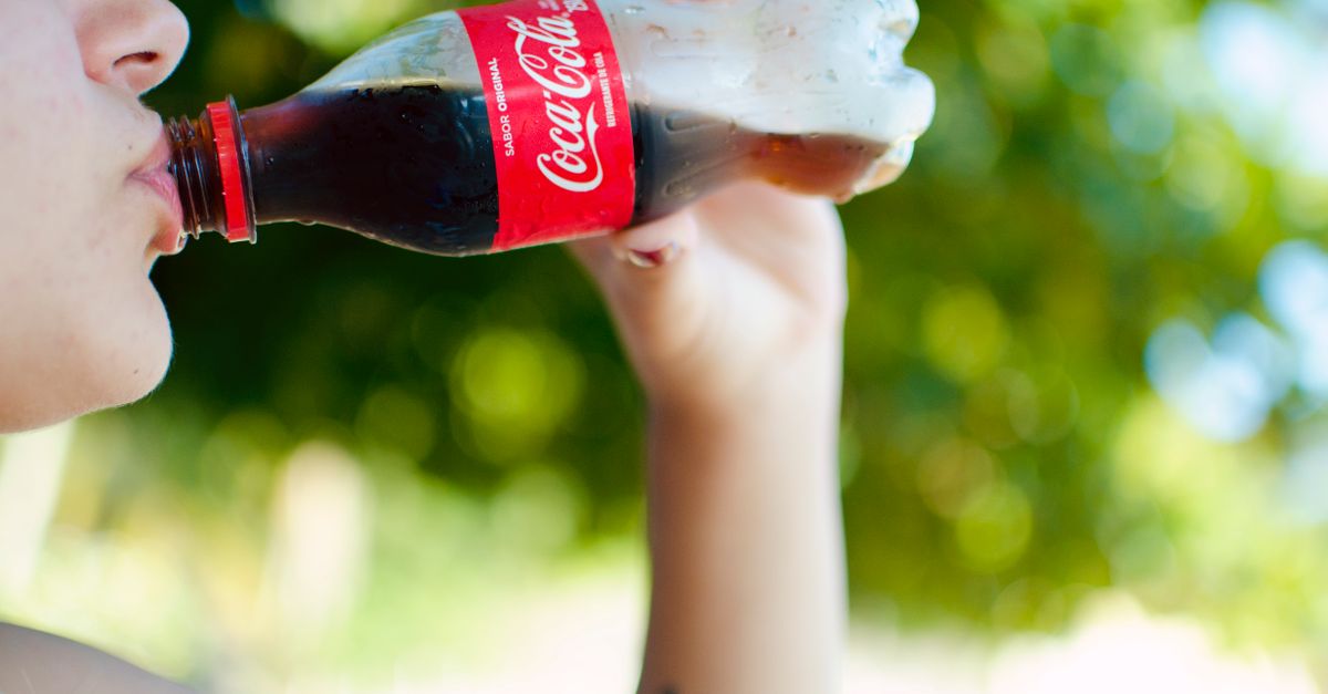 Um momento refrescante enquanto uma mulher bebe uma garrafa gelada de Coca Cola ao ar livre em um dia ensolarado.