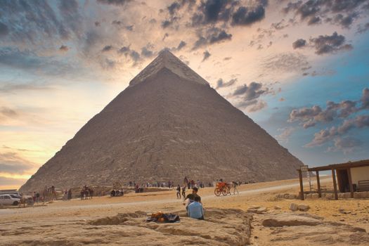A stunning view of the Great Pyramid of Giza during sunset with a dramatic sky and tourists in Cairo, Egypt.