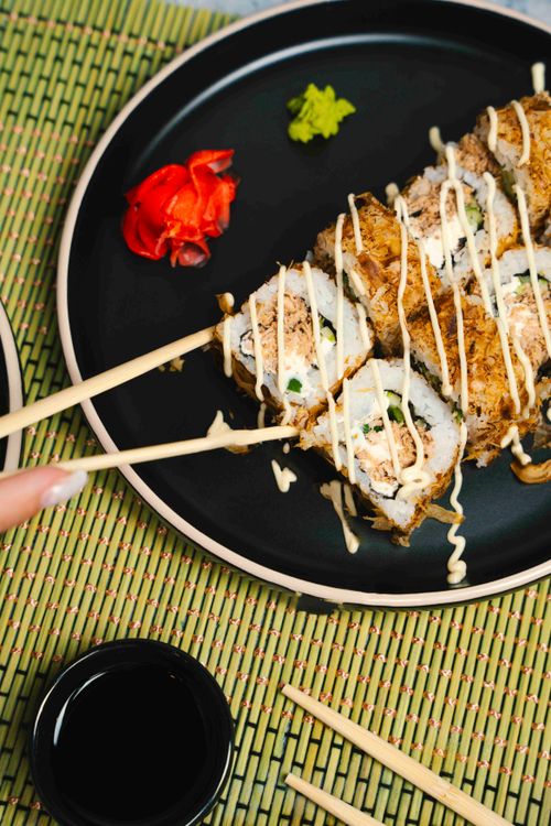 Free Close-up of sushi roll with chopsticks on a black plate, garnished with wasabi and ginger. Stock Photo