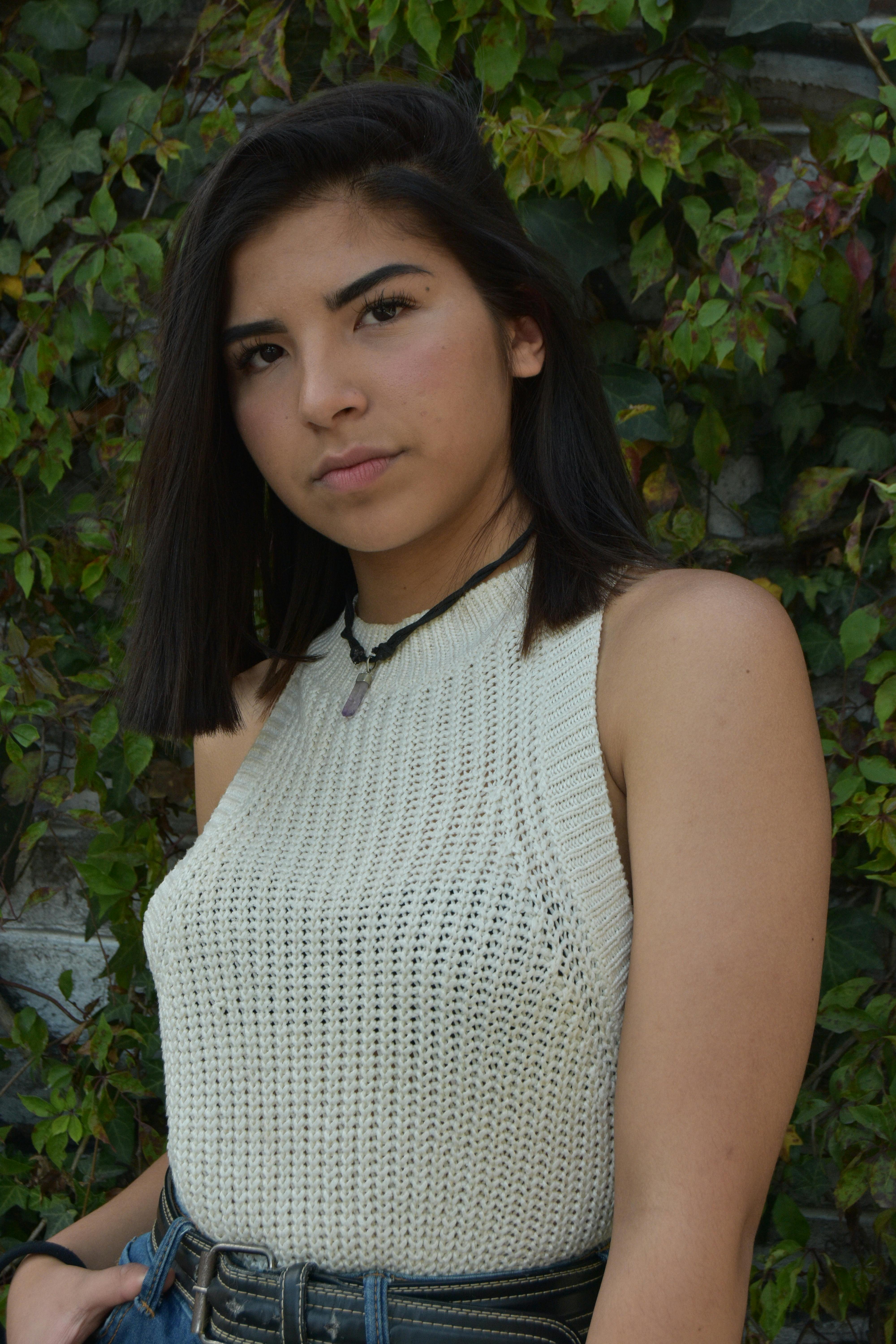 Stylish woman in a knitted halter top poses against a leafy background outdoors.