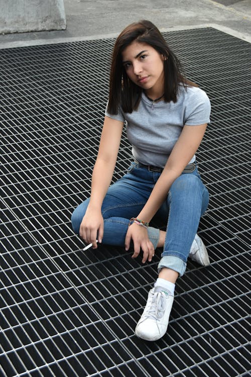 Young Brunette Woman with a Cigarette Sitting on a Steel Grating