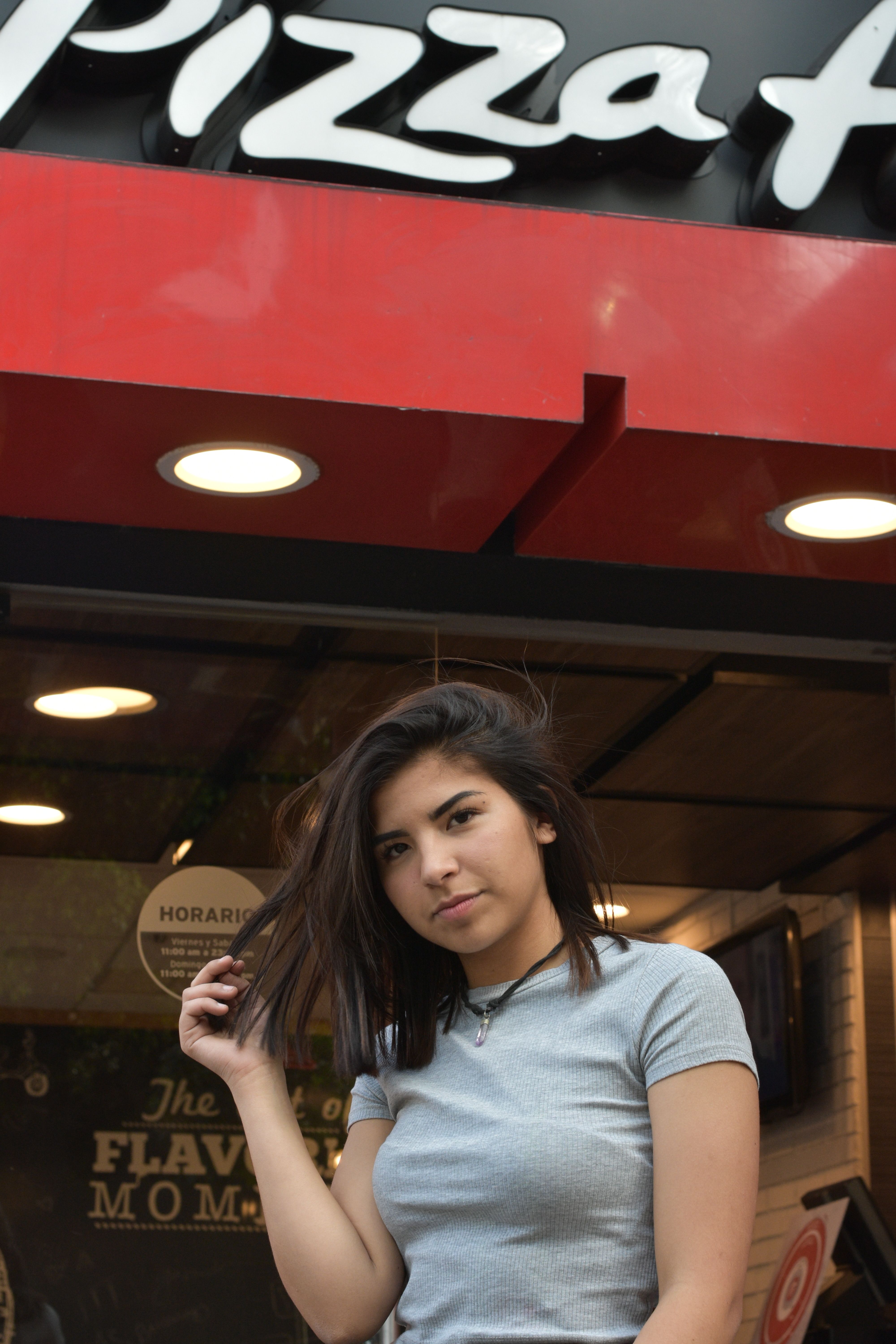 Young woman posing confidently outside a pizza restaurant, showcasing urban lifestyle.