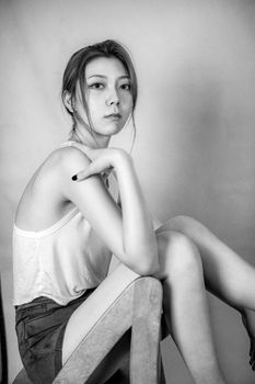Stylish black and white portrait of a young woman sitting on a chair in a studio setting.