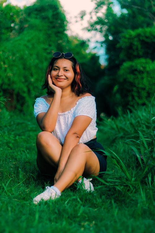 Free Smiling woman sitting on grass in a park, surrounded by lush greenery. Stock Photo