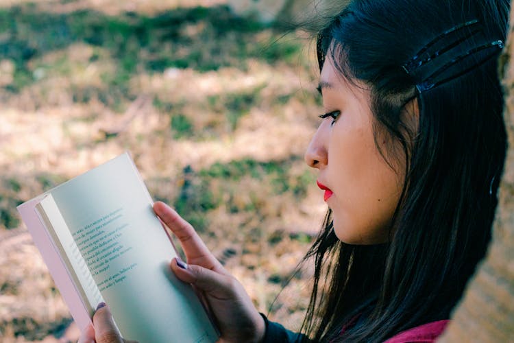 Young Woman Reading A Book In A Park 