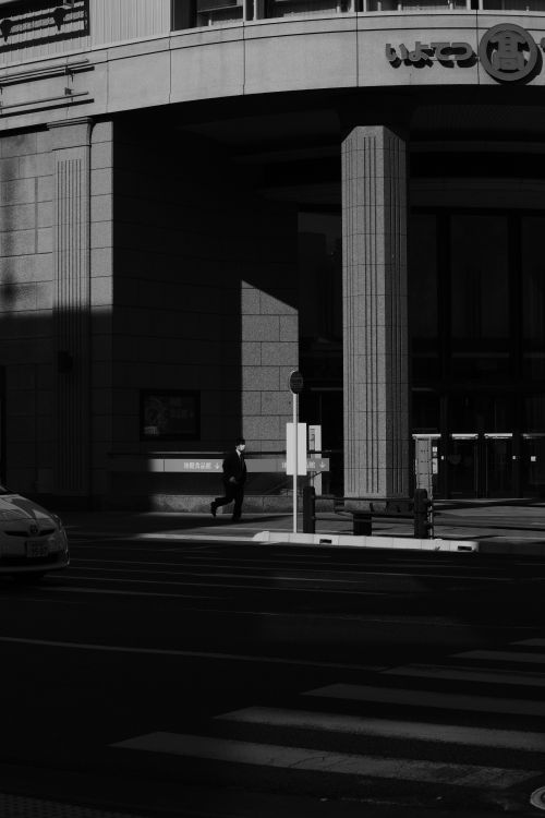 Free Black and white photo of a city street with a lone figure and dramatic shadows. Stock Photo