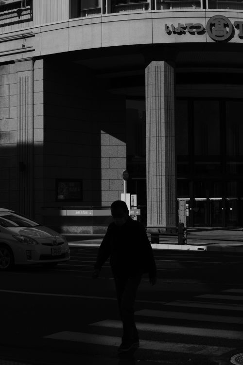 Free Silhouette of a person crossing a street against a city building backdrop. Stock Photo