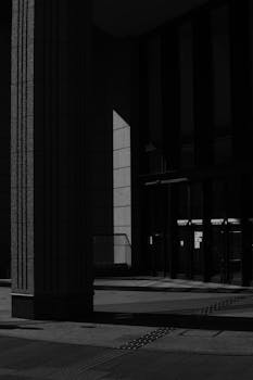 Monochrome urban architecture with dramatic shadows highlighting textured columns and glass facade.