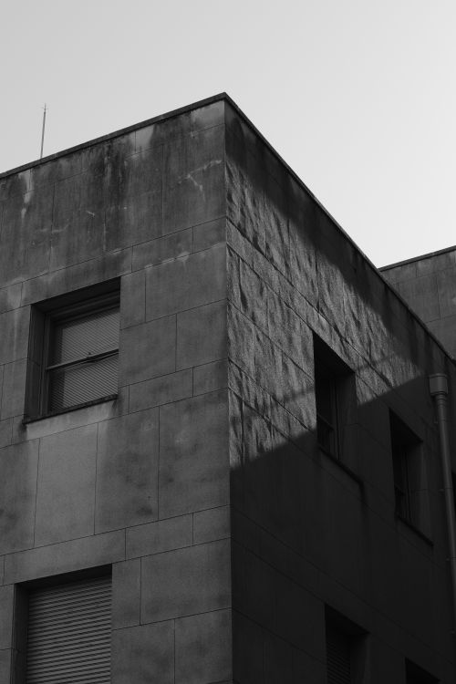 Free Black and white photo capturing a corner of a modern building with windows and shadows. Stock Photo