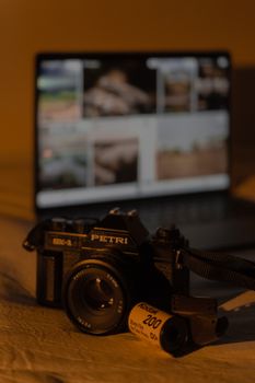Close-up of a vintage camera with film roll, laptop in background, warm tones.
