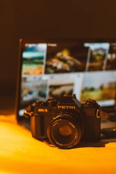 A classic film camera in front of a laptop screen, evoking nostalgia with warm tones.