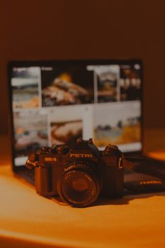 A vintage camera in front of a blurred laptop screen with warm lighting.