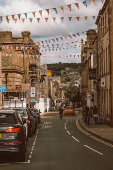 Quaint street in Lancaster, England with cars, cyclists, and historic architecture under festive bunting.