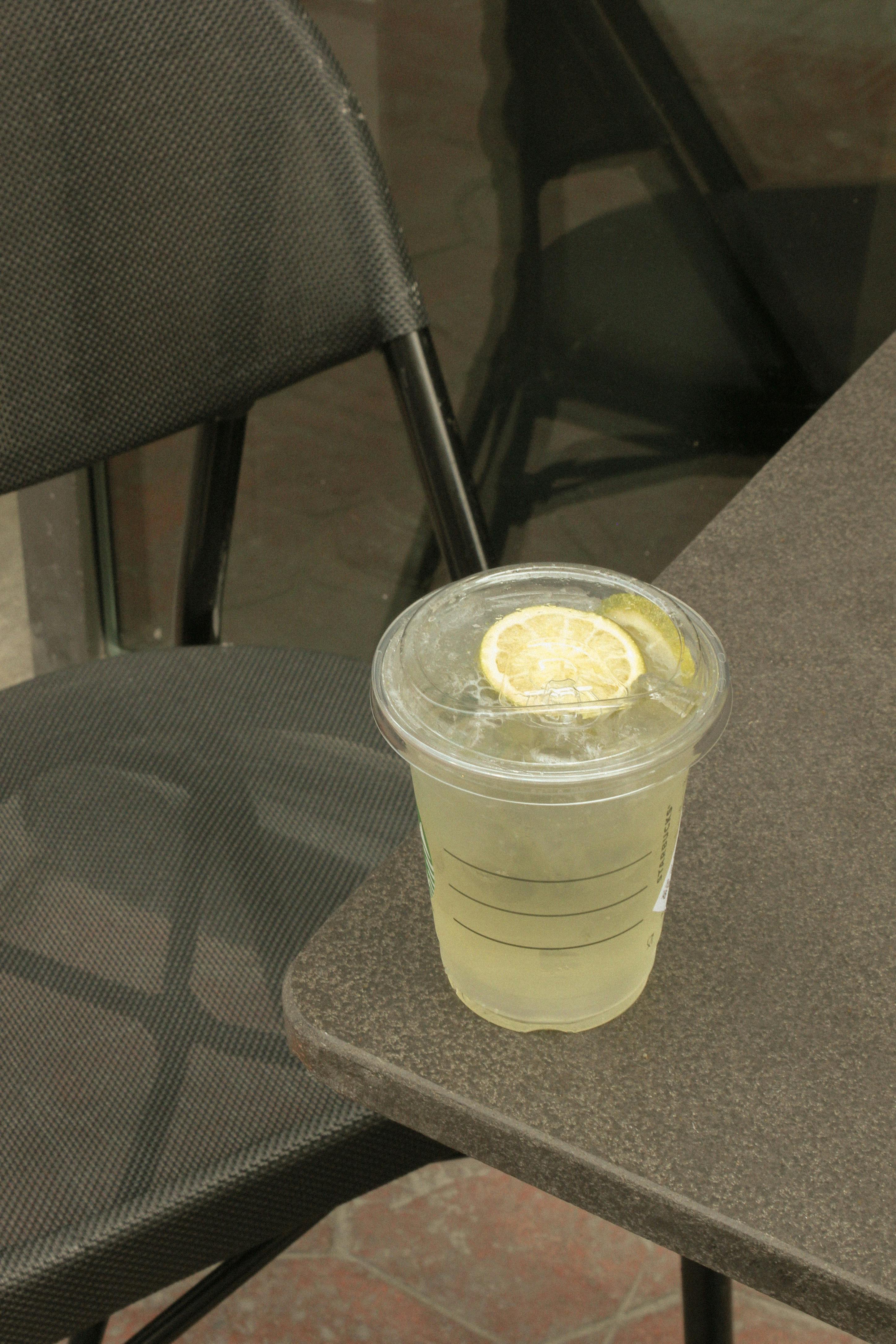 A refreshing lemonade with lemon slice on a takeout cup next to an outdoor cafe chair.