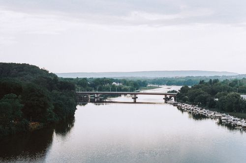 Free Scenic view of a river with bridges and boats surrounded by lush greenery under a cloudy sky. Stock Photo