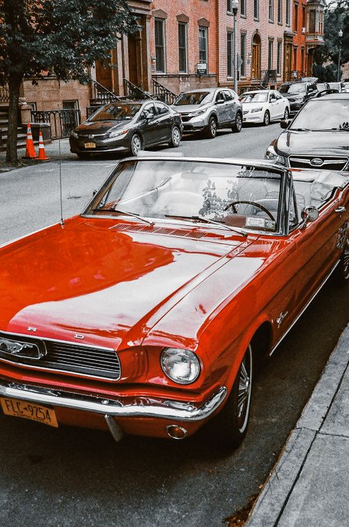 Free A vibrant red Ford Mustang convertible parked on a city street, showcasing vintage automotive charm. Stock Photo