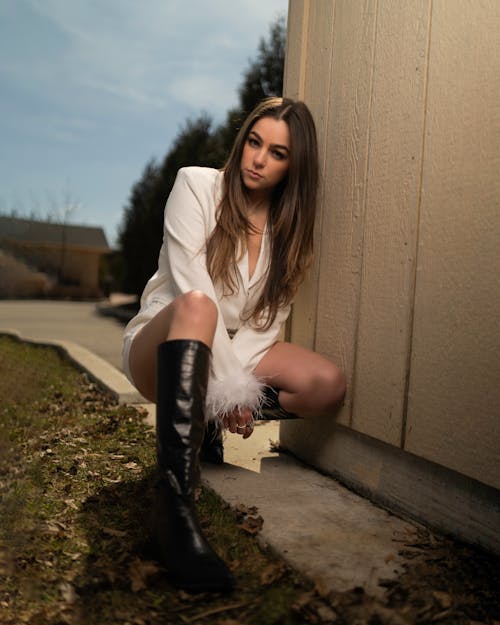 A woman in white boots and a white jacket leaning against a wall