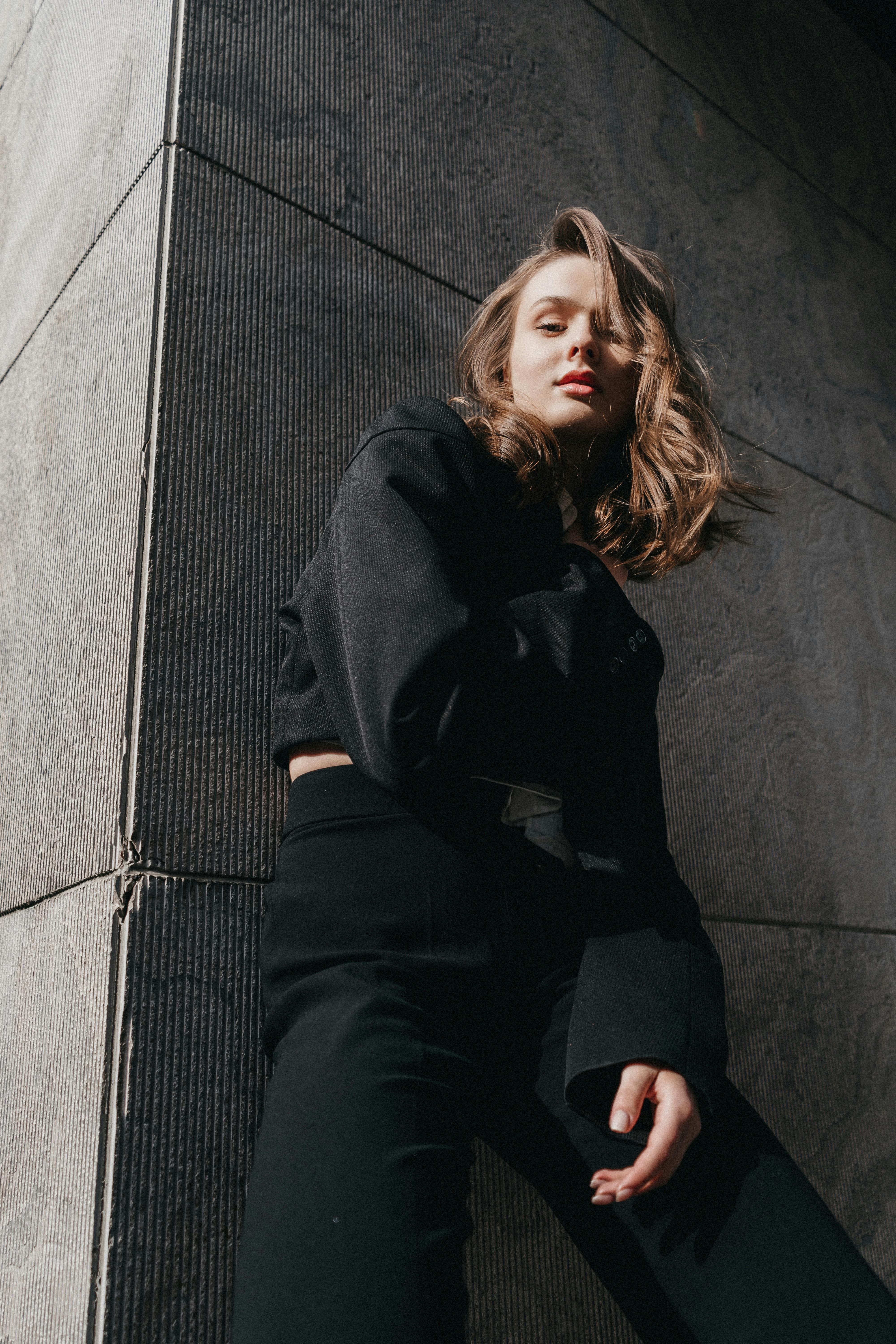 a woman in black pants and a black top leaning against a wall