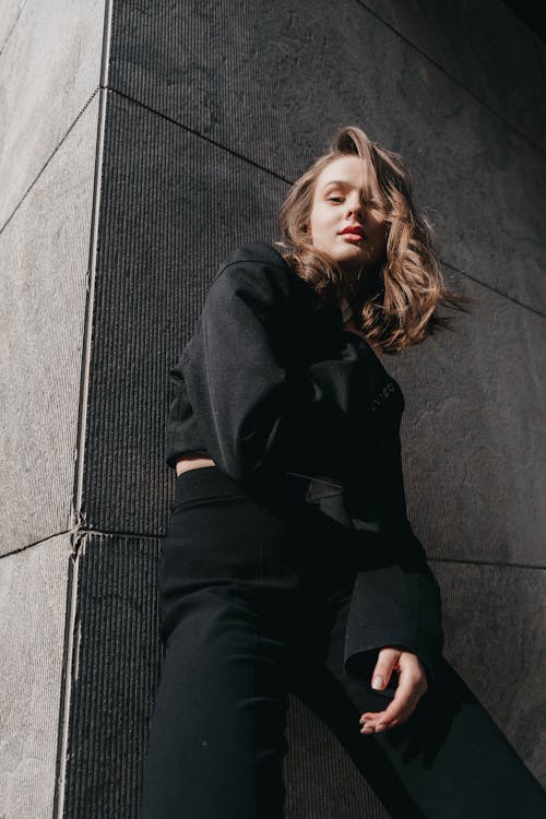 Free A woman in black pants and a black top leaning against a wall Stock Photo