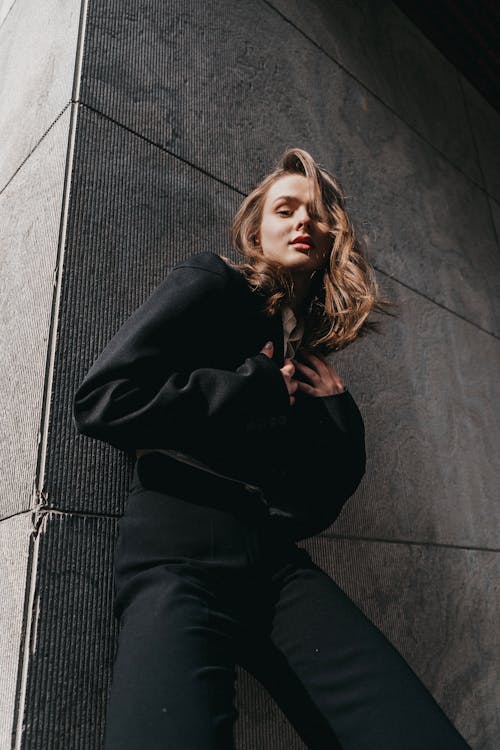 Free A woman in black pants leaning against a wall Stock Photo