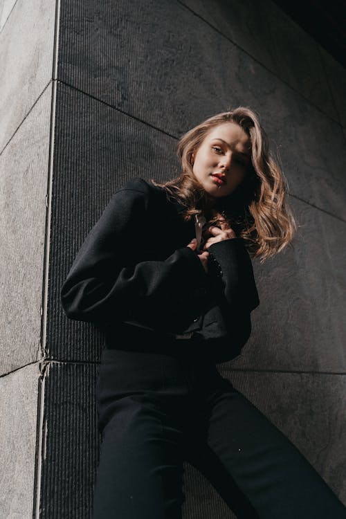 A woman leaning against a wall wearing black pants