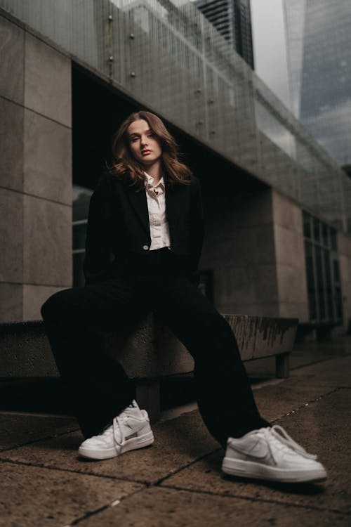 A woman in a suit and sneakers sitting on a bench