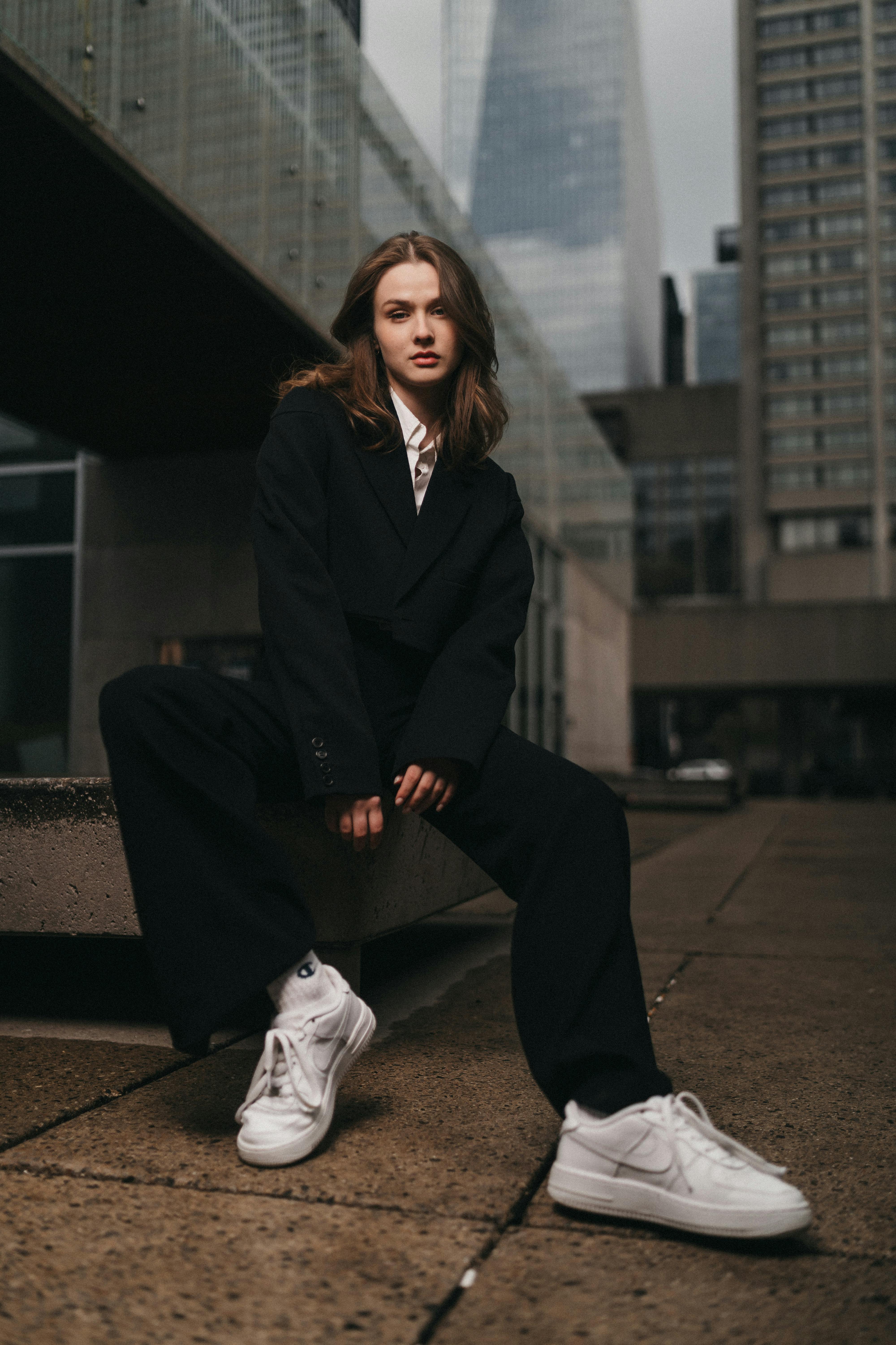 a woman in a black suit and white sneakers sitting on a bench