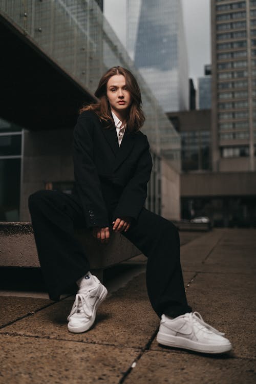 A woman in a black suit and white sneakers sitting on a bench
