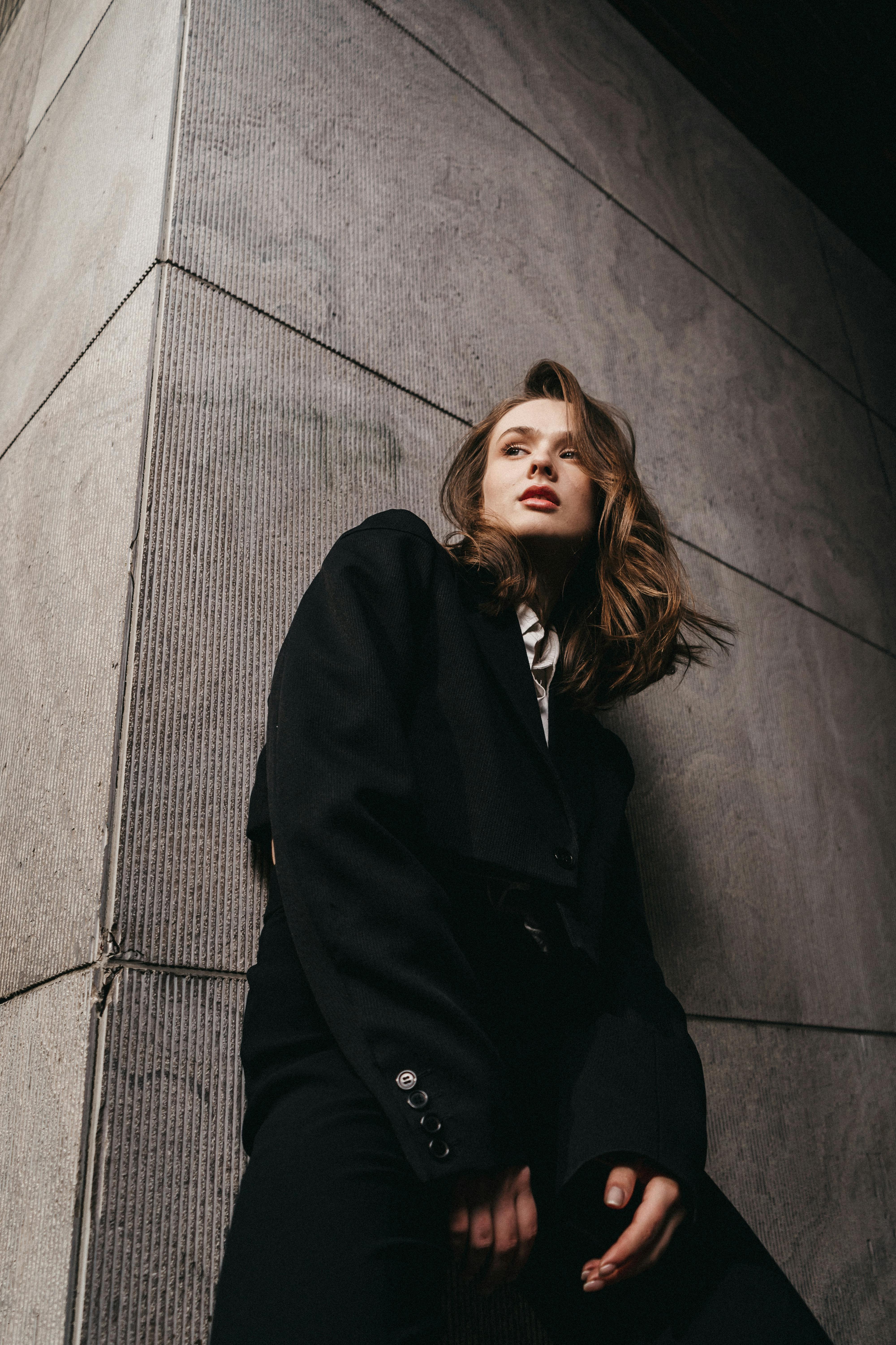 a woman leaning against a wall wearing a black jacket