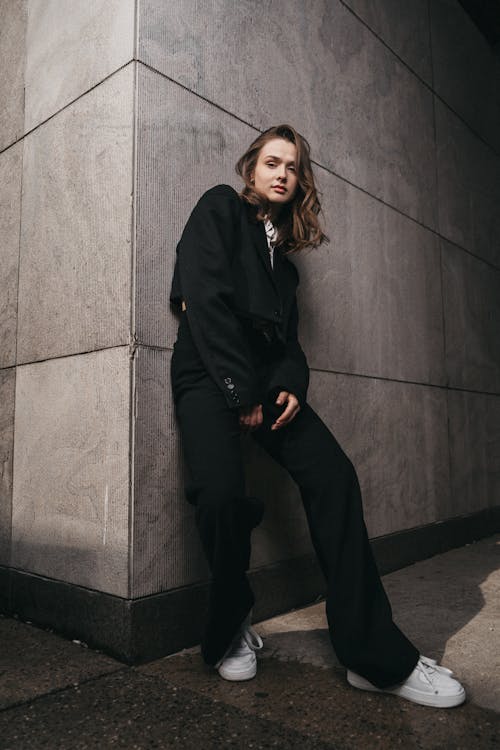 Free A woman in black pants and jacket leaning against a wall Stock Photo