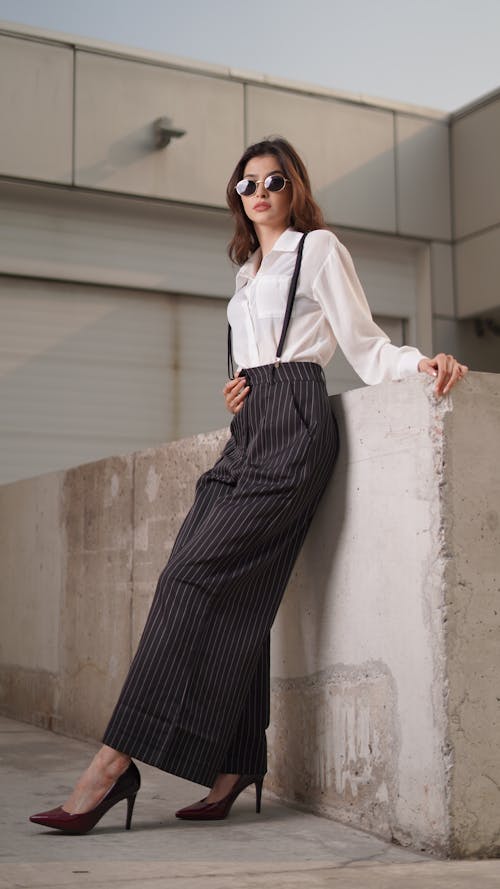 Free A woman in a white shirt and black pants leaning against a wall Stock Photo