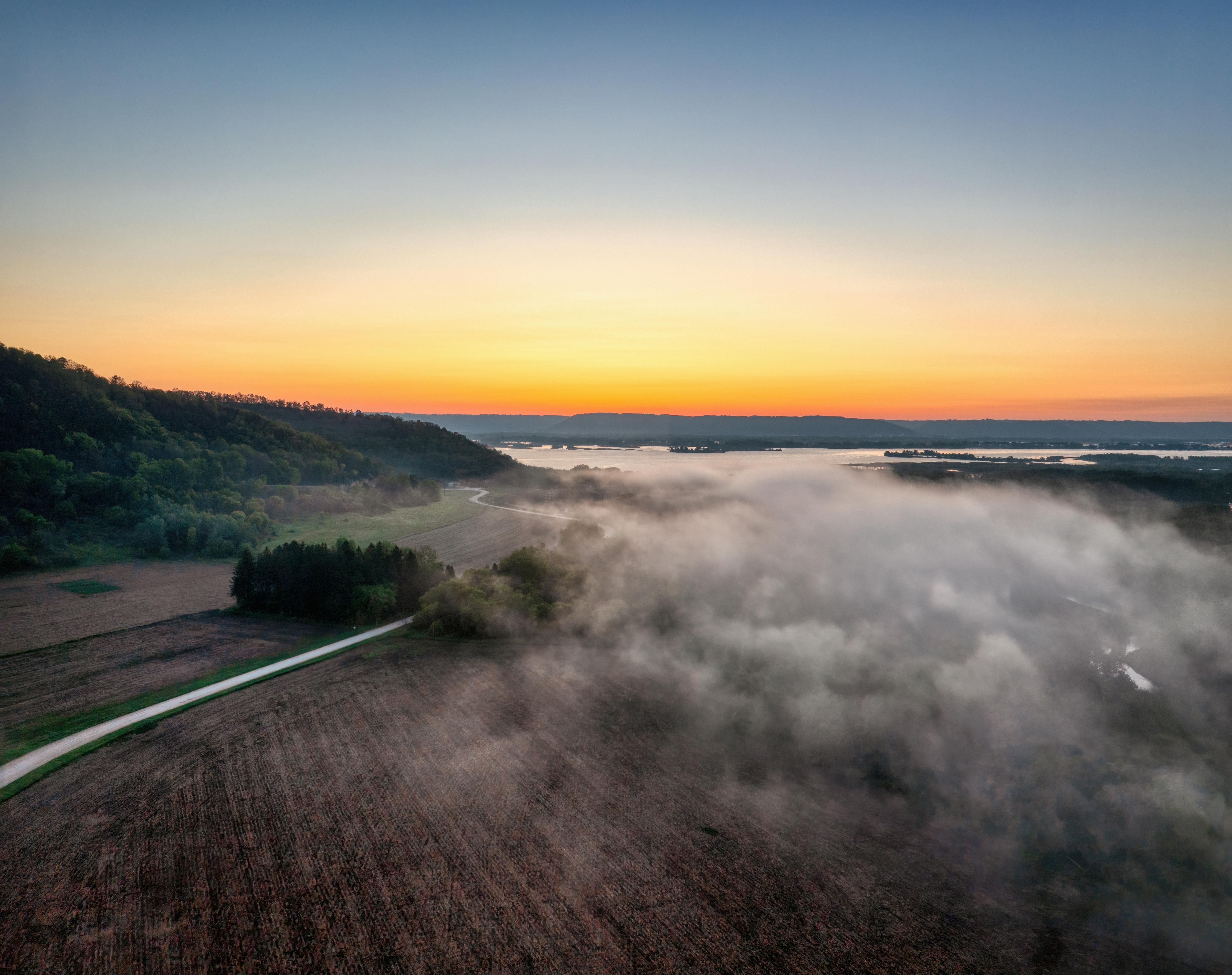 Aerial view of misty fields at sunrise in Weaver, Minnesota, showcasing serene rural landscape.