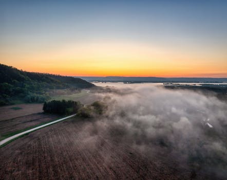 Aerial view of misty fields at sunrise in Weaver, Minnesota, showcasing serene rural landscape.