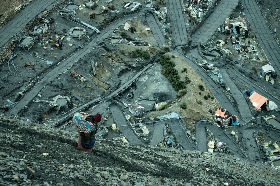 A woman walks on a rocky path overlooking a rugged mining site in the Andes.