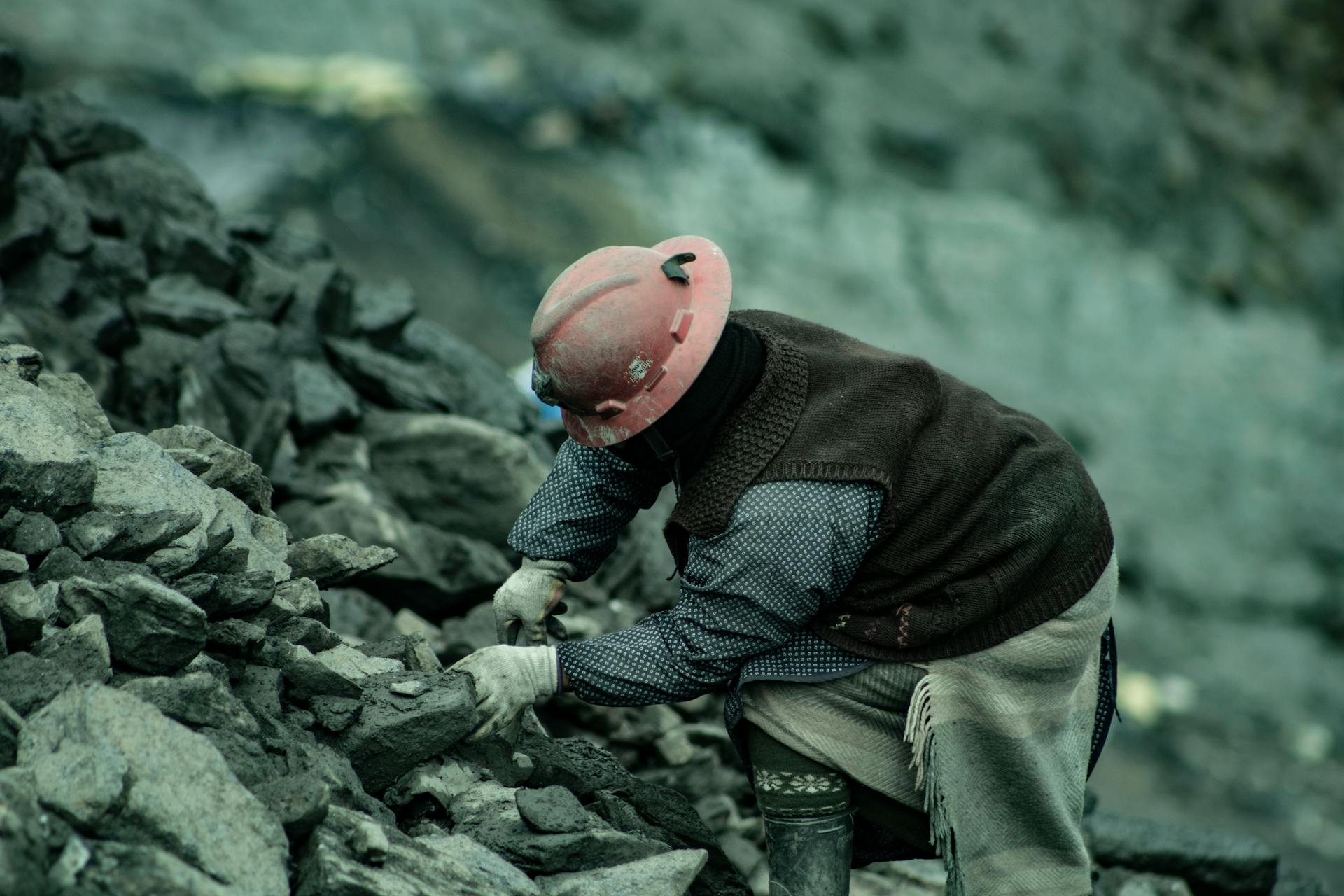 A coal miner in a hard hat working amidst rocky terrain, emphasizing labor and resilience.