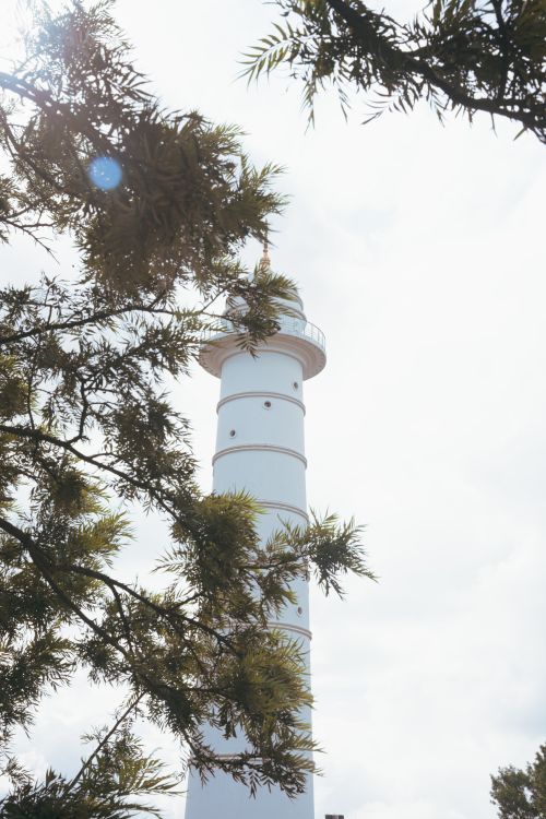 Free A white lighthouse amidst tree branches, under a bright sky in Kathmandu, Nepal. Stock Photo