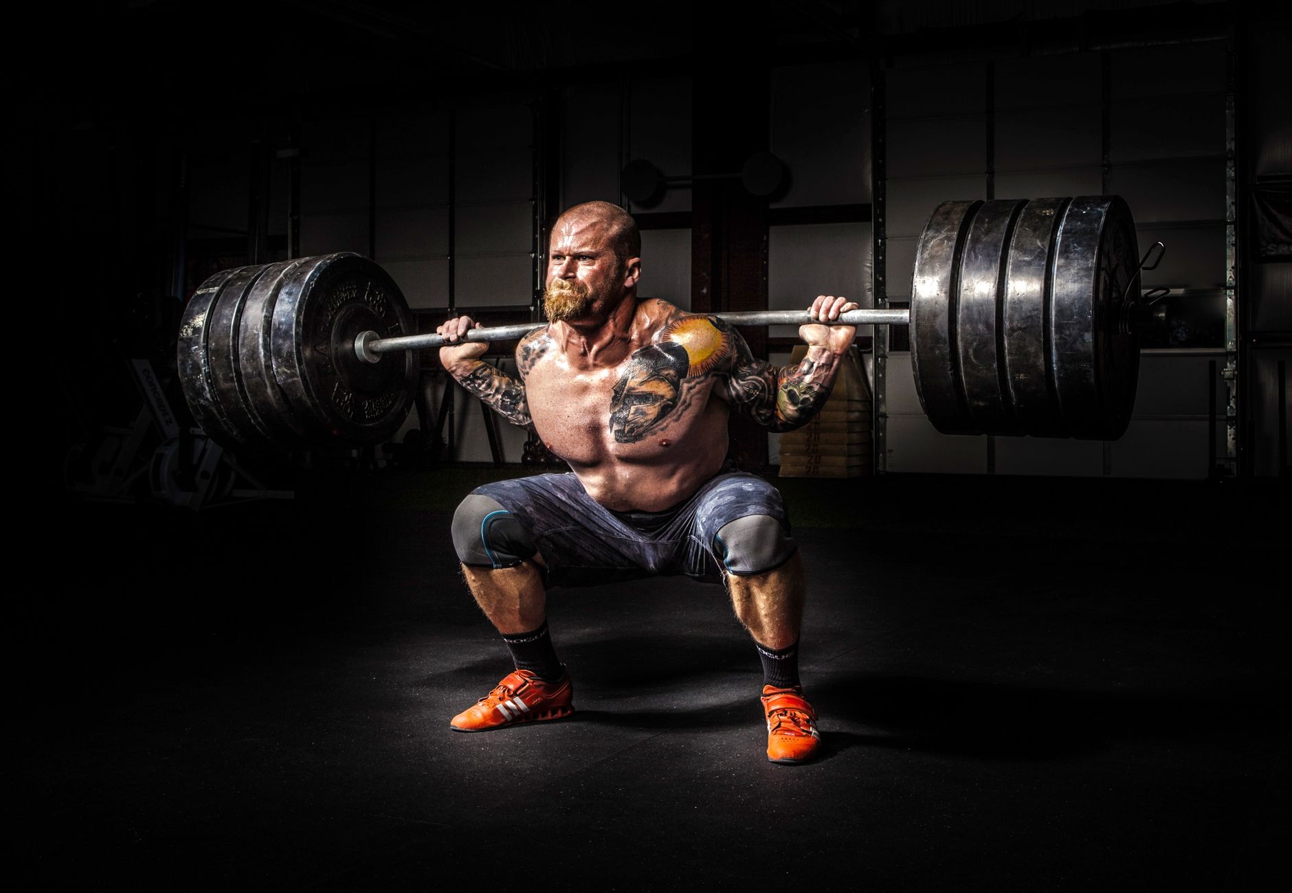 Muscular man lifting heavy weights during an intense squat session inside a gym.