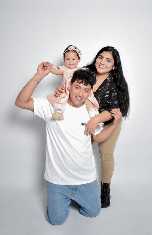Free Smiling family of three posing in a studio shot with father, mother, and baby daughter. Stock Photo