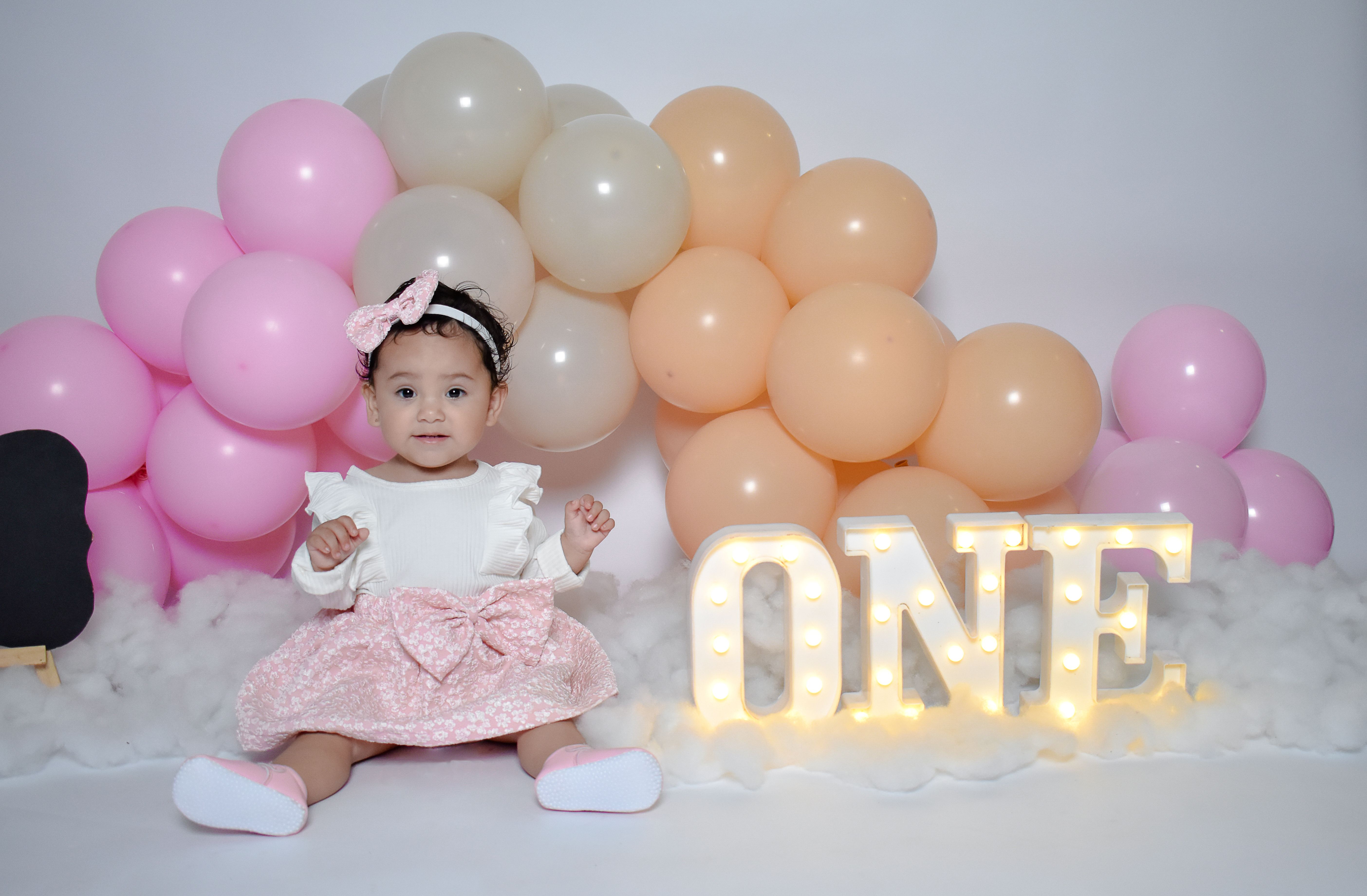 Charming first birthday setup with balloons and a smiling baby girl in a pink dress.