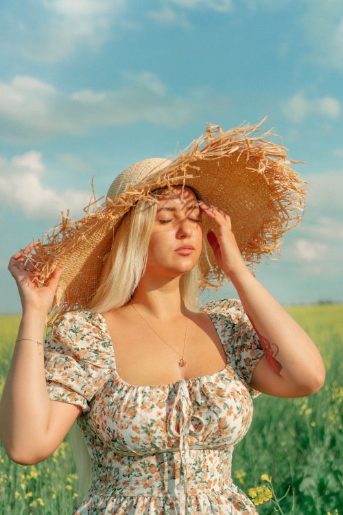 Free Woman in floral dress and wicker hat enjoying the sunny countryside. Perfect summer vibe. Stock Photo