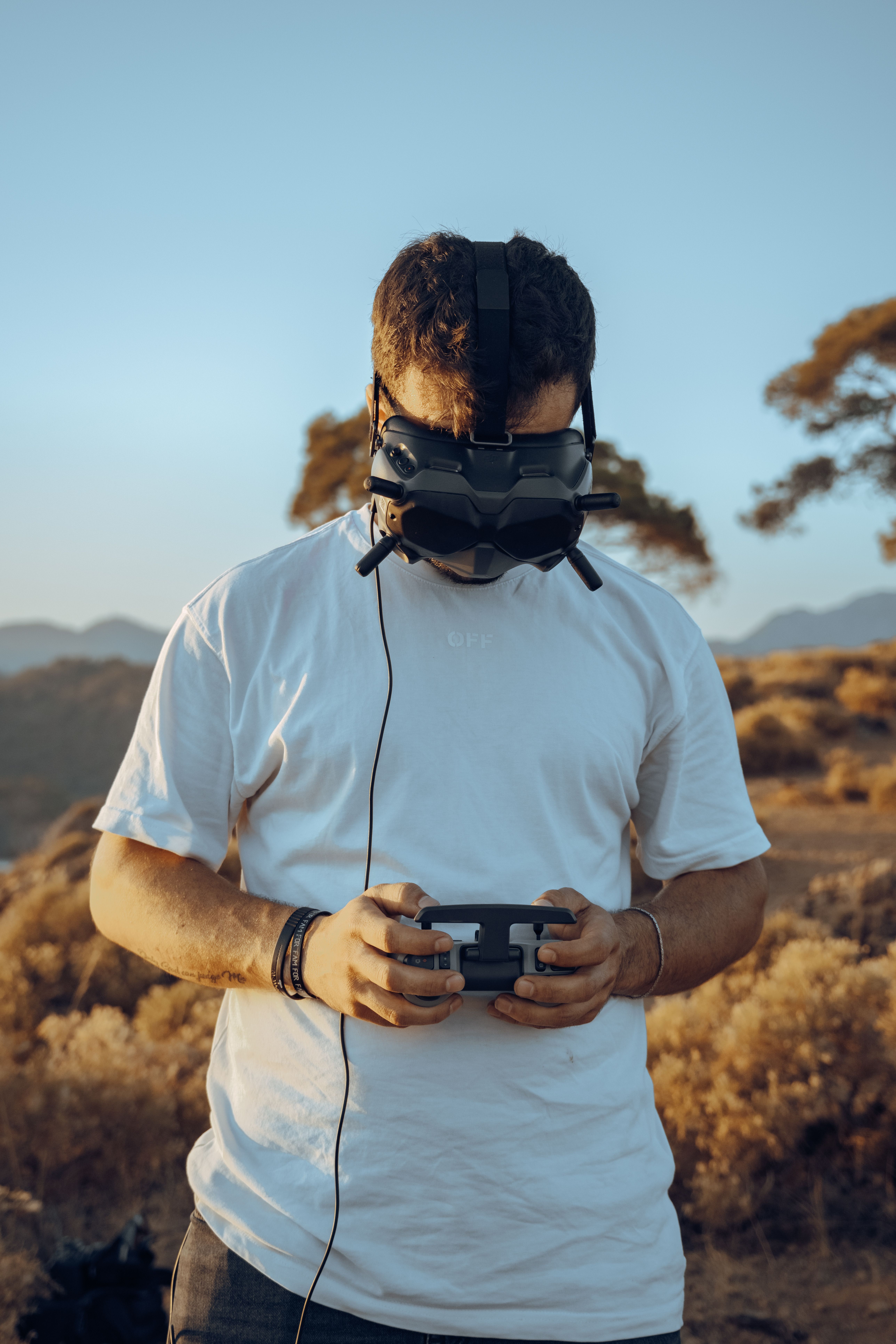 A man controls a drone using VR goggles and a controller in a scenic outdoor setting.